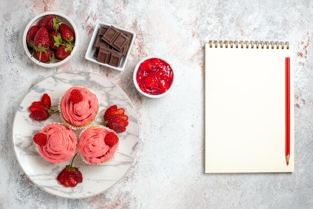 Vista superior de pasteles de fresa rosa con mermelada y barras de chocolate sobre superficie blanca