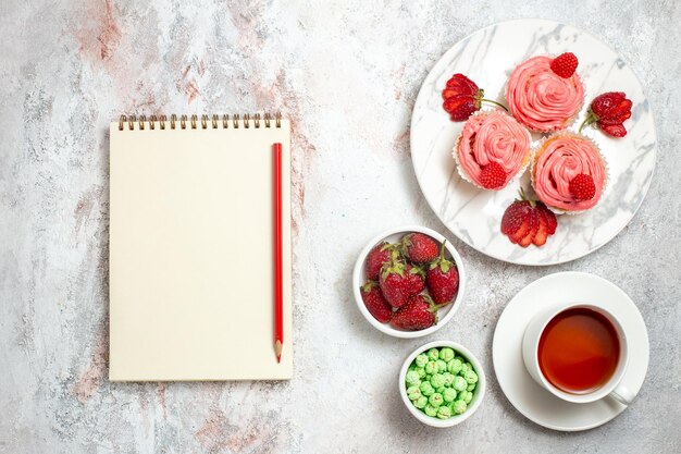 Vista superior de pasteles de fresa rosa con té en superficie blanca