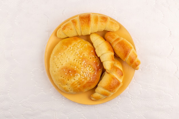 Vista superior pasteles junto con croissants dentro de la placa naranja en el piso blanco