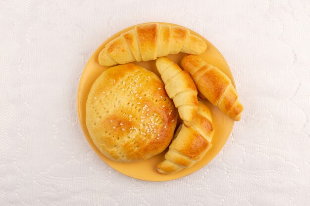 Vista superior pasteles junto con croissants dentro de la placa naranja en el piso blanco