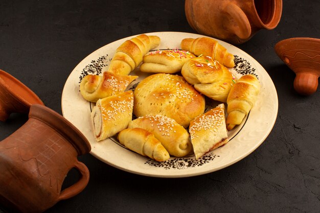 Vista superior pasteles junto con croissants dentro de un plato blanco sobre el fondo oscuro