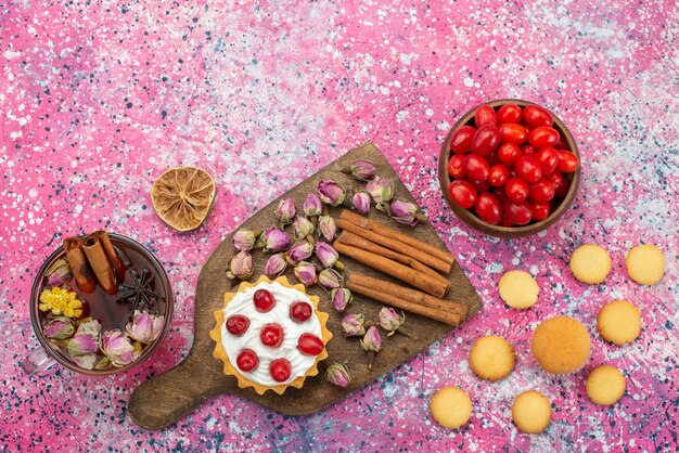 Vista superior de pastelito con crema junto con té de galletas de canela y frutos rojos en la superficie púrpura fruta dulce