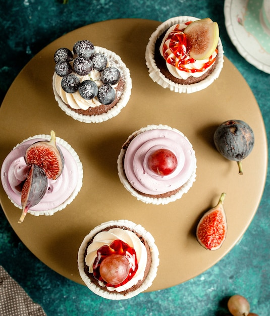 Foto gratuita vista superior de pastelitos de chocolate decorados con crema de vainilla, higos, uvas y arándanos