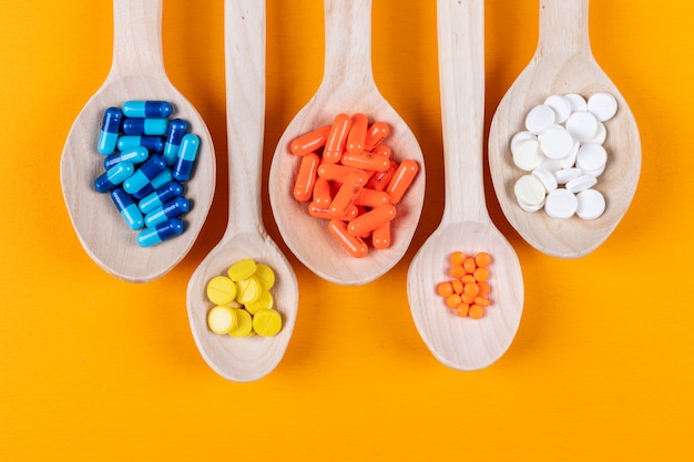Vista superior de pastillas de colores en cucharas de madera sobre fondo naranja. horizontal