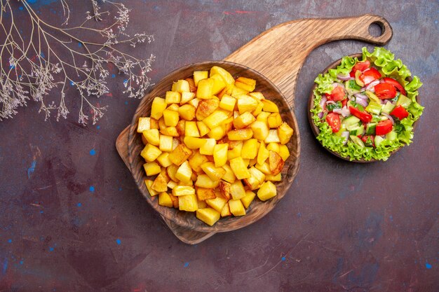 Vista superior de patatas cocidas en rodajas con ensalada de verduras en la oscuridad