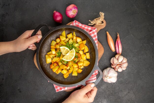 Vista superior de patatas fritas dentro de la sartén con limón sobre el fondo oscuro