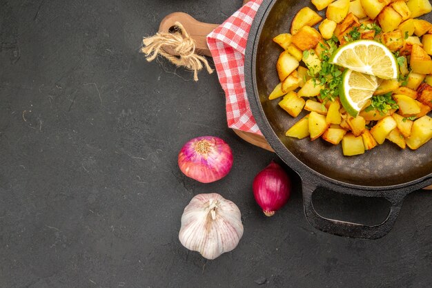 Vista superior de patatas fritas dentro de la sartén con limón sobre el fondo oscuro