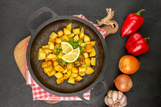 Vista superior de patatas fritas dentro de la sartén con limón y verduras sobre fondo oscuro