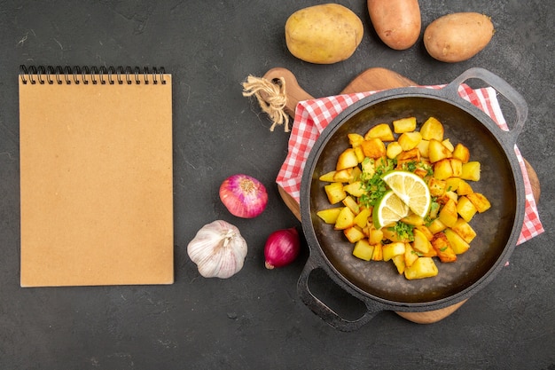 Vista superior de patatas fritas dentro de la sartén con verduras frescas sobre fondo oscuro