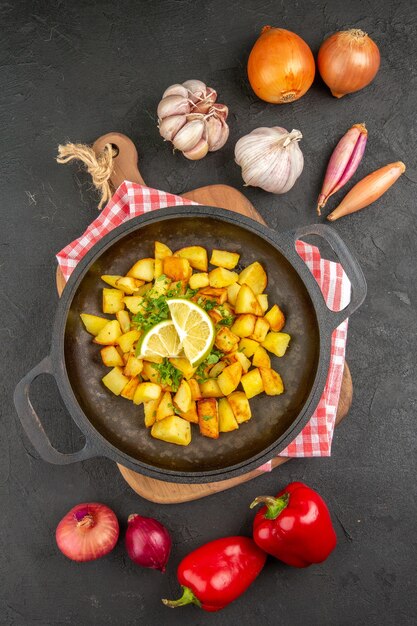 Vista superior de patatas fritas dentro de la sartén con verduras sobre fondo gris oscuro