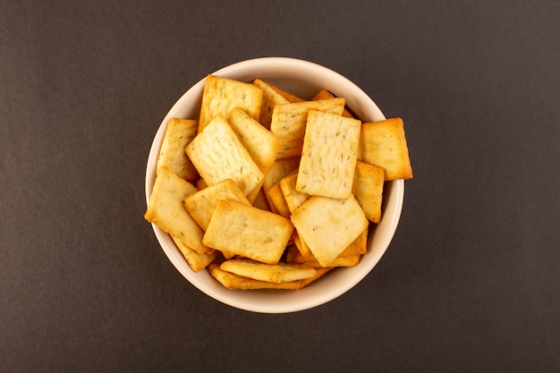 Una vista superior patatas fritas saladas sabrosas galletas de queso dentro de un plato blanco sobre el fondo oscuro bocadillo sal comida crujiente
