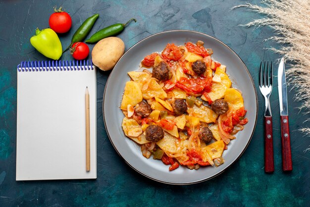 Vista superior de patatas en rodajas cocidas con albóndigas y verduras cocidas en el escritorio azul oscuro.