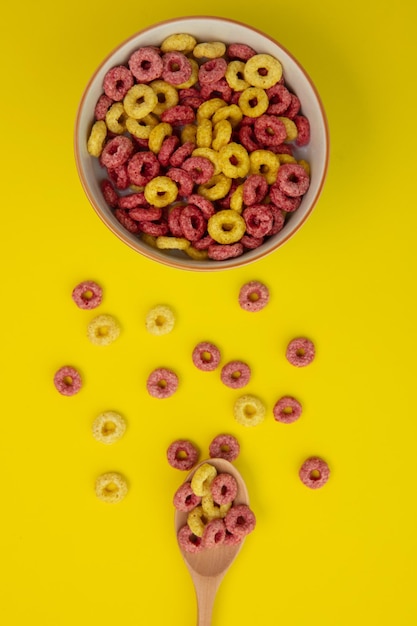 Vista superior del patrón de cereales con cucharada de cereales y tazón de cereales sobre fondo amarillo