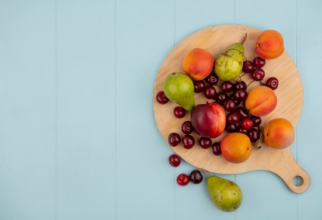 Vista superior del patrón de frutas como cereza melocotón pera albaricoque en tabla de cortar y sobre fondo azul con espacio de copia