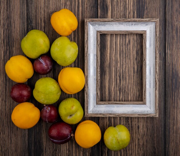 Vista superior del patrón de frutas como pluots y nectacots con marco sobre fondo de madera con espacio de copia