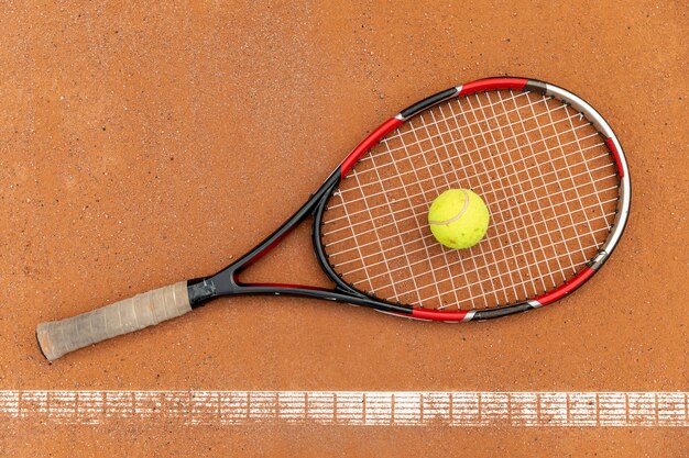 Vista superior pelota de tenis con raqueta en el suelo