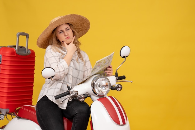 Vista superior del pensamiento joven con sombrero y sentado en una motocicleta y sosteniendo el mapa concentrado en algo en amarillo