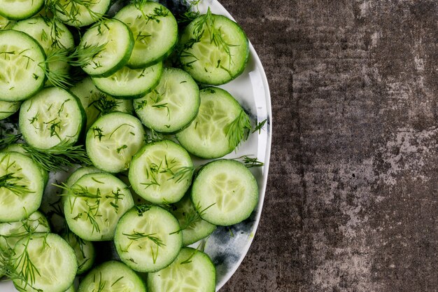 Vista superior de pepino en rodajas en un plato con eneldo con espacio de copia a la derecha en piedra marrón