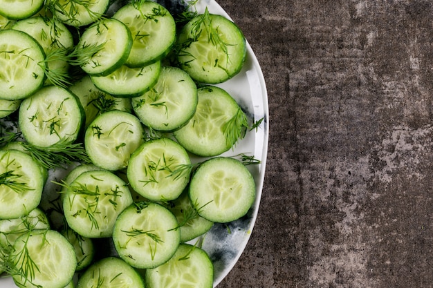 Vista superior de pepino en rodajas en un plato con eneldo con espacio de copia a la derecha en piedra marrón