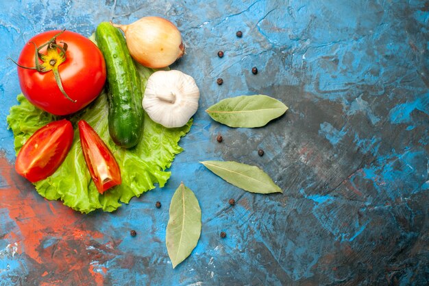 Vista superior de pepino de verduras frescas con ensalada de tomate y ajo sobre fondo azul.