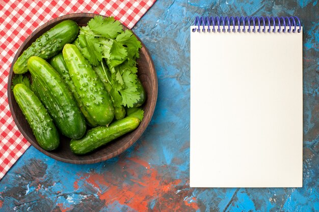 Vista superior de pepinos frescos dentro de la placa con el bloc de notas sobre fondo azul foto de salud comida madura ensalada de color dieta de alimentos