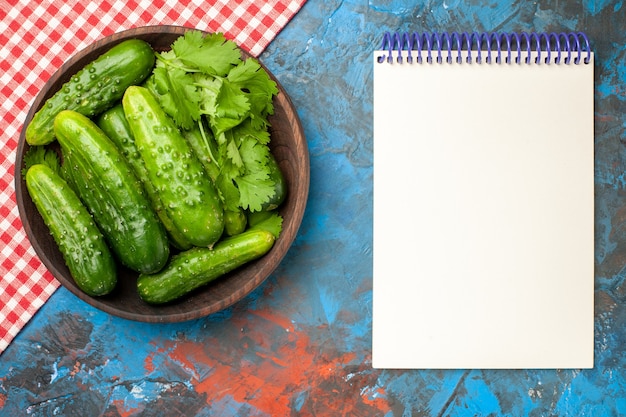 Vista superior de pepinos frescos dentro de la placa con el bloc de notas sobre fondo azul foto de salud comida madura ensalada de color dieta de alimentos