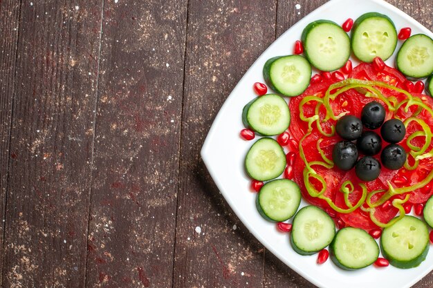 Vista superior de pepinos en rodajas con aceitunas dentro de la placa en un escritorio rústico marrón dieta ensalada verduras vitamina salud