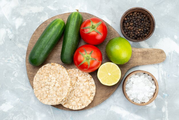 Vista superior de pepinos y tomates con limas y galletas redondas en gris