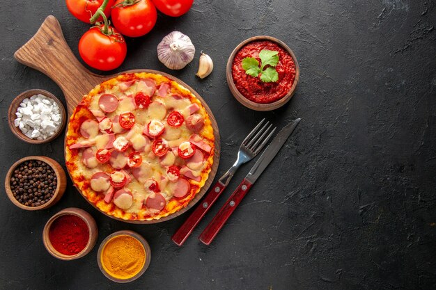 Vista superior pequeña pizza deliciosa con tomates y condimentos en la mesa oscura