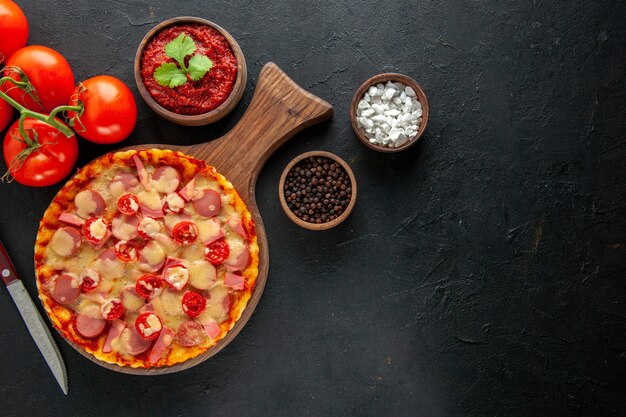 Vista superior pequeña pizza deliciosa con tomates rojos frescos en la mesa oscura