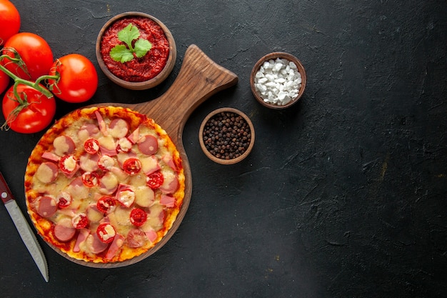 Vista superior pequeña pizza deliciosa con tomates rojos frescos en la mesa oscura