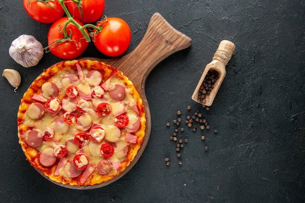 Vista superior pequeña pizza deliciosa con tomates rojos frescos en la mesa oscura