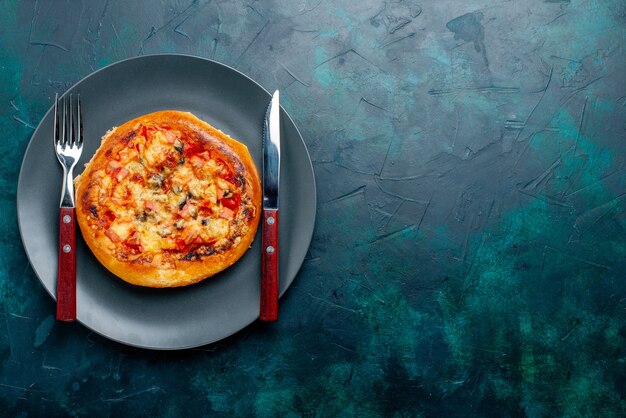 Vista superior de la pequeña ronda de pizza de queso formada con cubiertos en la superficie azul oscuro