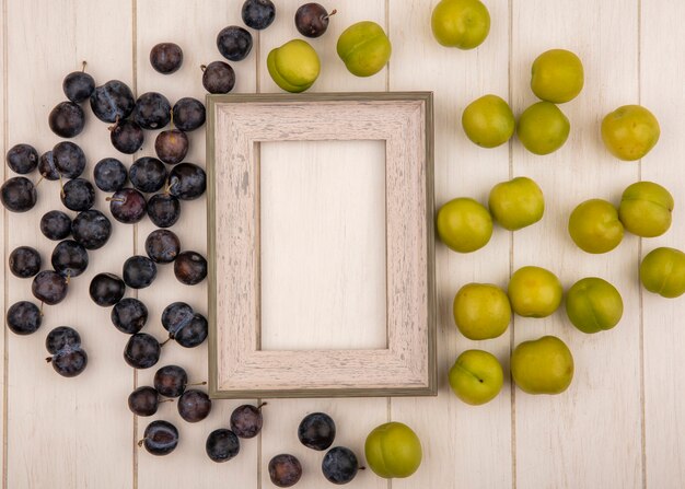 Vista superior de las pequeñas endrinas de fruta amarga azul-negra y ciruela cereza verde aislado sobre un fondo blanco de madera con espacio de copia