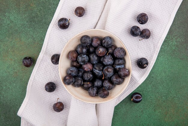 Vista superior de las pequeñas endrinas de fruta amarga azul-negra en un recipiente blanco sobre un mantel sobre un fondo verde