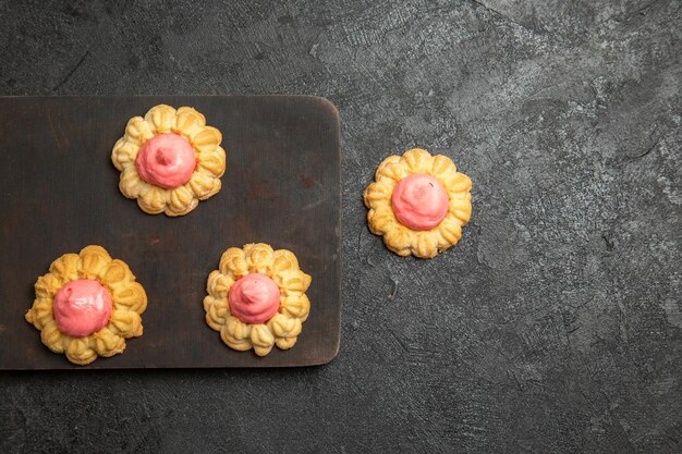 Vista superior de pequeñas galletas de azúcar con crema de fresa en la superficie gris