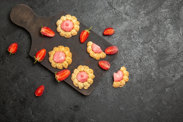 Vista superior de pequeñas galletas de azúcar con crema de fresa en la superficie gris