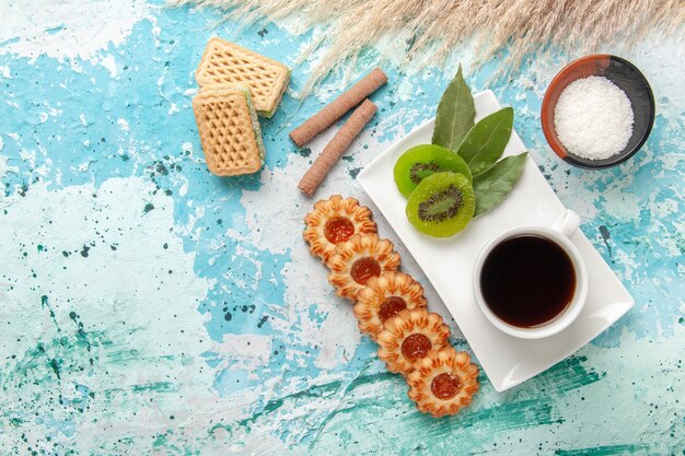 Vista superior pequeñas galletas de azúcar con una taza de té y gofres sobre fondo azul claro pastel hornear galleta dulce azúcar pastel té