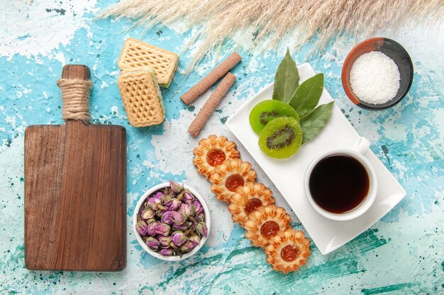 Vista superior de pequeñas galletas de azúcar con una taza de té y waffles en el pastel de escritorio azul claro hornear galletas pastel de azúcar dulce té