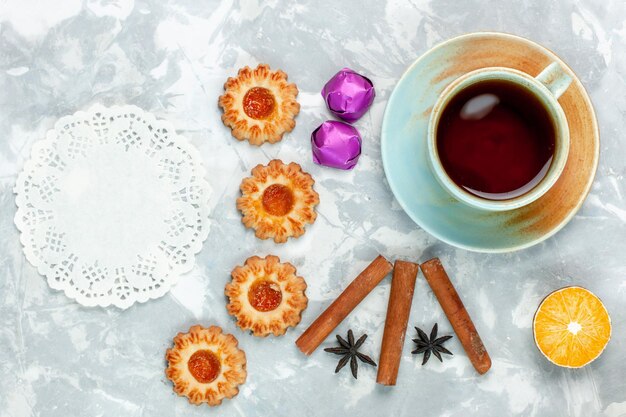 Vista superior de pequeñas galletas con canela y té sobre una superficie blanca clara