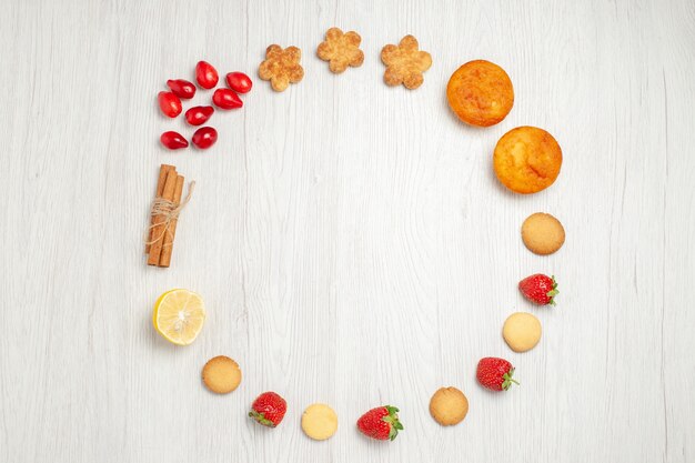 Vista superior pequeñas galletas con frutas en el escritorio blanco