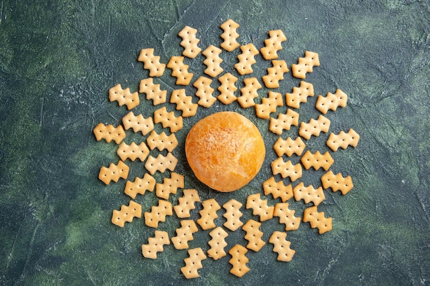 Vista superior de pequeñas galletas saladas con pastelito sobre superficie oscura