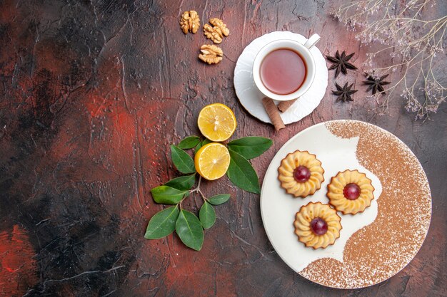 Vista superior pequeñas galletas con taza de té en el dulce pastel de galletas de azúcar de mesa oscura