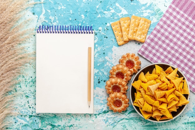 Vista superior pequeñas patatas fritas picantes dentro de la placa con galletas saladas y galletas en el escritorio de color azul claro chips de calorías crujientes de color snack