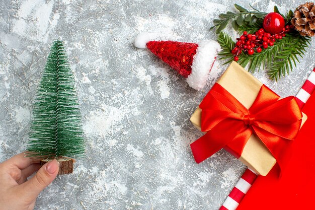 Vista superior pequeño árbol de Navidad en mano femenina pequeño sombrero de santa presente en el espacio libre de la mesa blanca gris