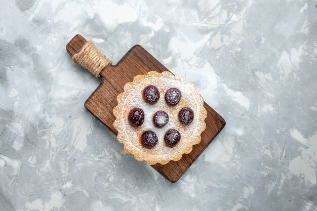 Foto gratuita vista superior del pequeño pastel de azúcar en polvo con cerezas en el escritorio de luz, pastel de galletas dulces de azúcar de café