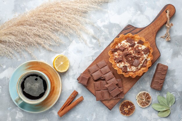 Vista superior de un pequeño pastel de crema con barras de chocolate y té en la mesa de luz, pastel dulce, crema de azúcar, chocolate