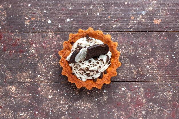 Vista superior del pequeño pastel con crema y chocolate aislado en marrón de madera, bizcocho de galleta dulce hornear
