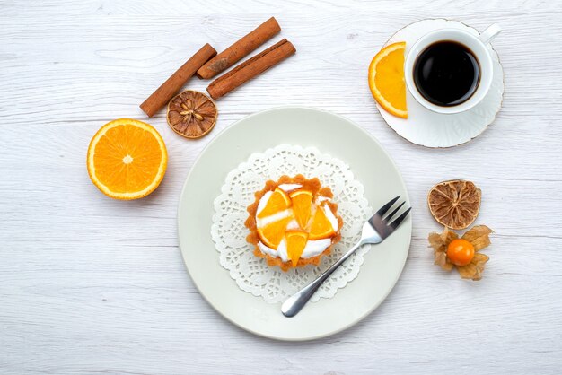 Vista superior del pequeño pastel con crema y naranjas en rodajas junto con café y canela en la mesa de luz, pastel de frutas, galleta, azúcar dulce