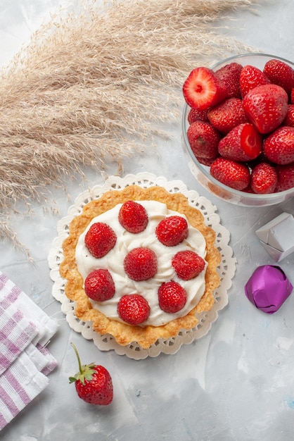 Vista superior pequeño pastel cremoso con fresas rojas frescas y pastel de dulces de chocolate en la mesa de luz blanca pastel crema de galletas de frutas y bayas